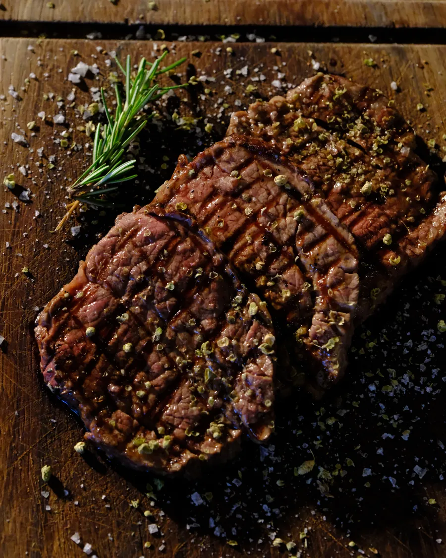 Sliced grilled steak with rosemary on a wooden board